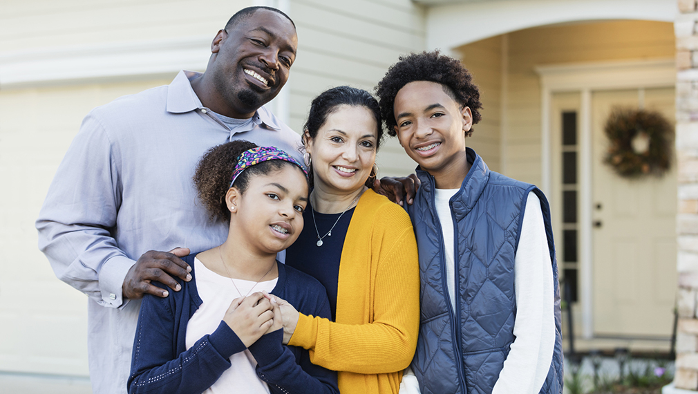 A family of four standing in front of their home.